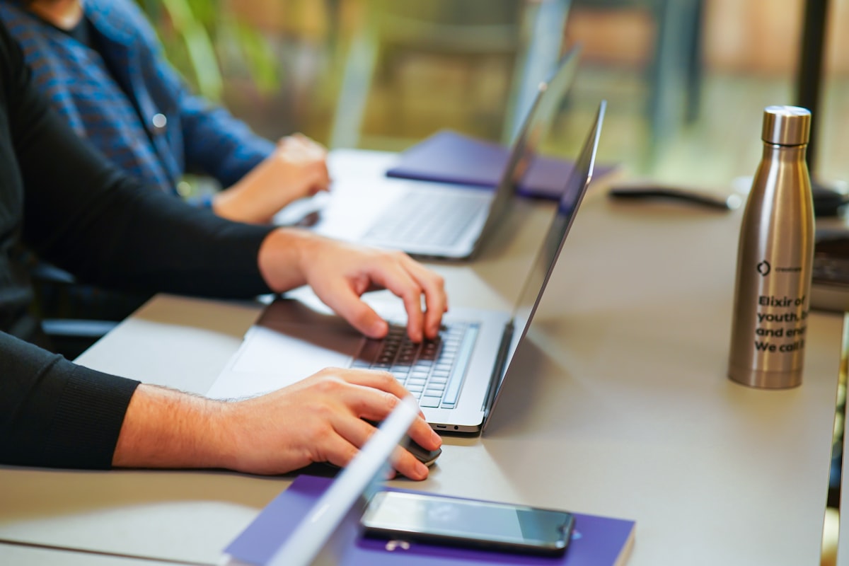 Two people working on laptops at an office table, collaborating on a project